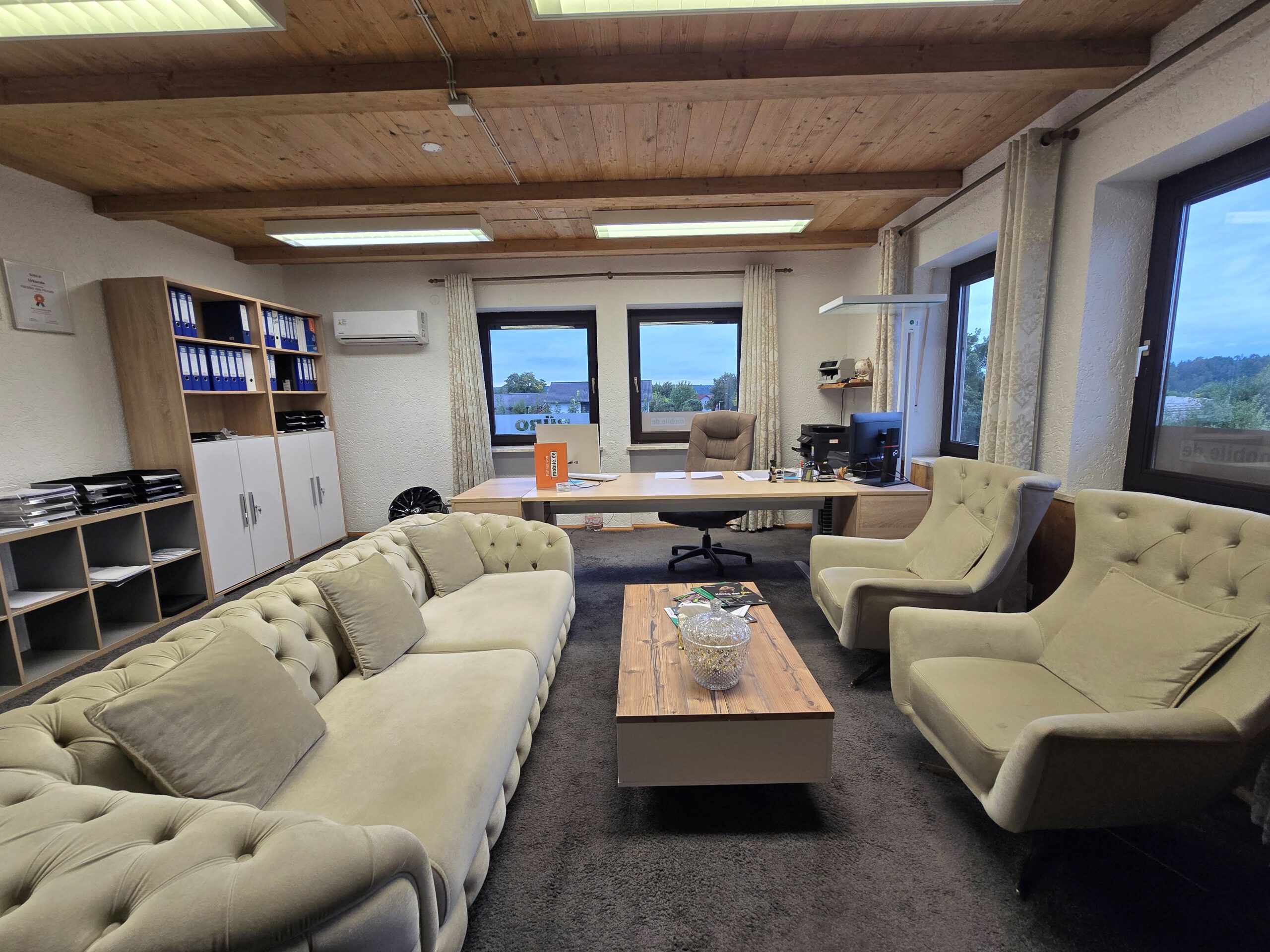 Gemütlich eingerichtetes Büro mit Sofa, Sesseln, Schreibtisch und Blick nach draußen.