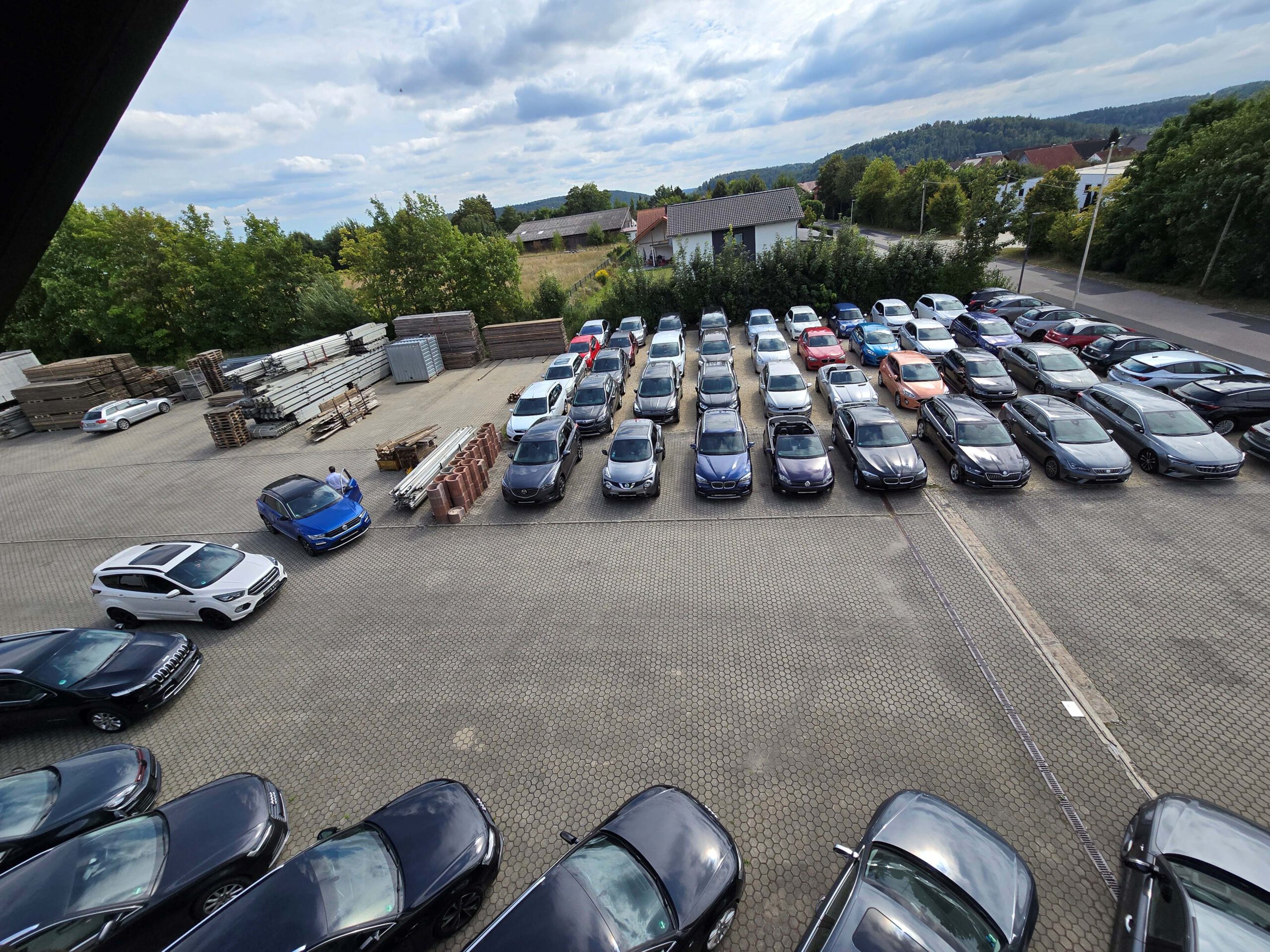 Überblick über den großen Parkplatz des Autohauses, auf dem zahlreiche Fahrzeuge in Reihen stehen.